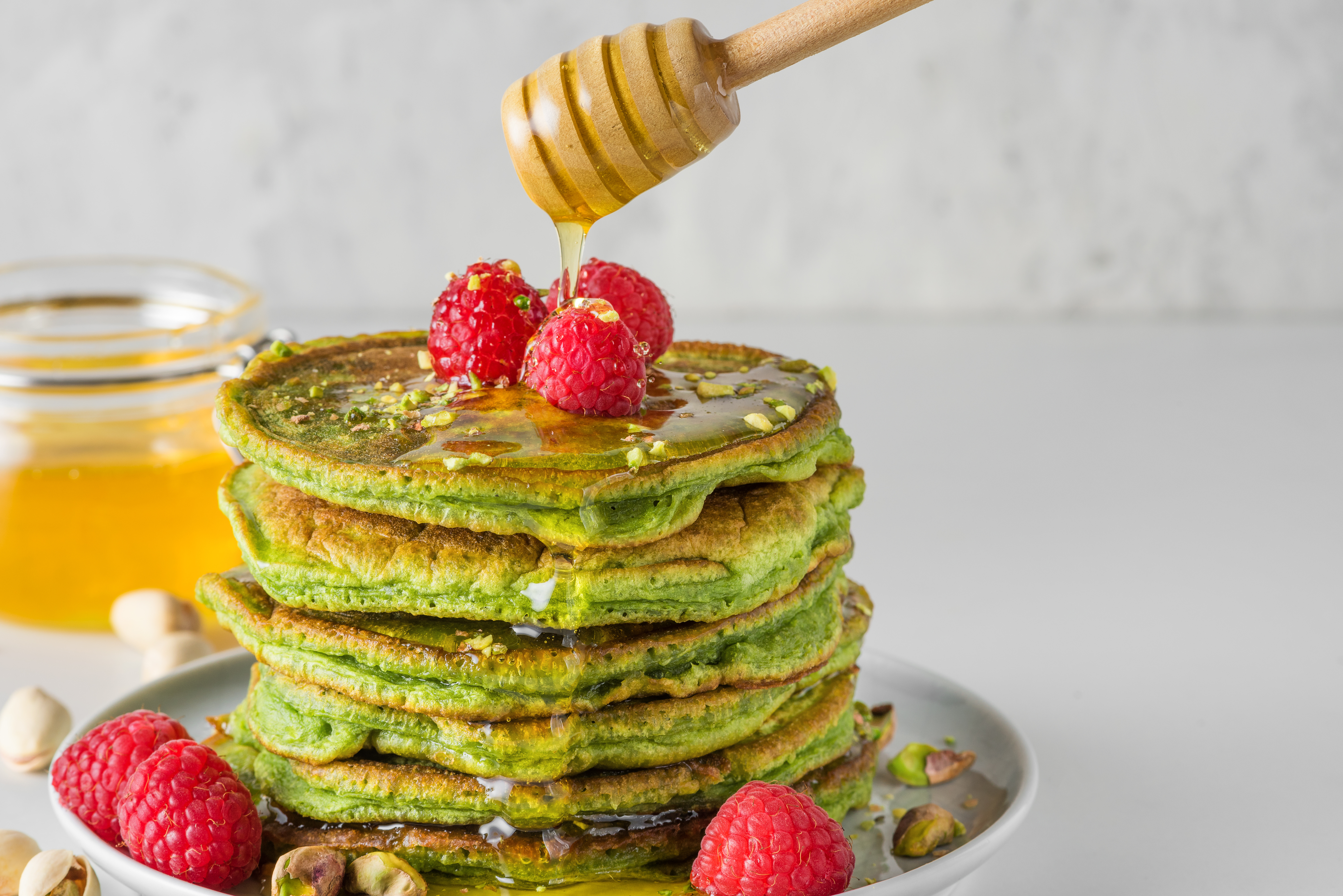 Matcha tea pancakes with fresh raspberries, pistachios and flowing honey.
