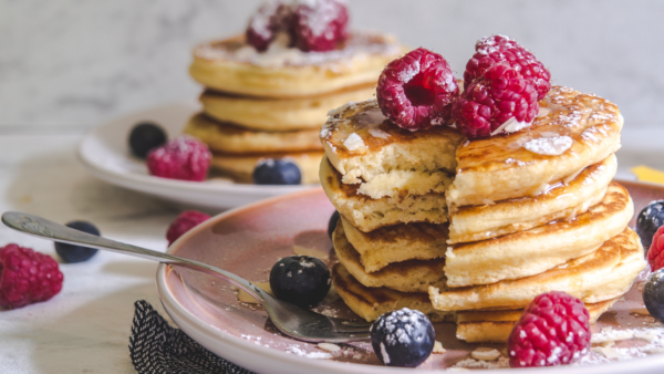 Stacks of fluffy early grey pancakes on pink plates with blueberries and raspberries.