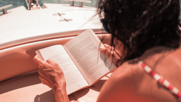 Woman reading a book on a boat at sea in the sunshine.