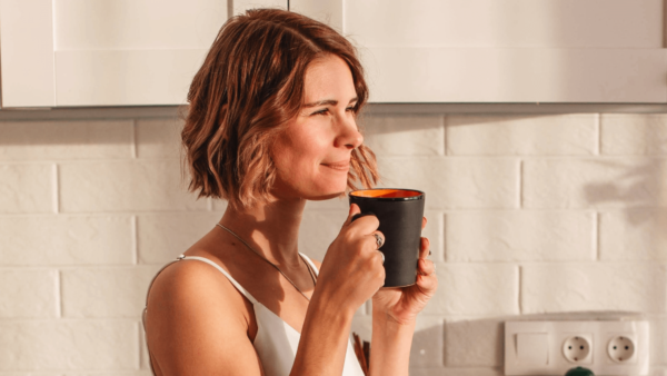 Woman drinking mug of tea in kitchen.